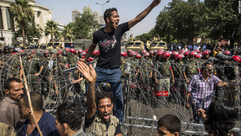 A protester stands on a barricade of barbed wire as Egyptian military police stand guard. Egypt&#39;s Supreme Constitutional Court ruled that the Islamist-led parliament must be immediately dissolved.
