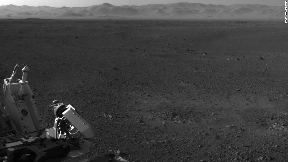 This image, with a portion of the rover in the corner, shows the wall of &quot;Gale Crater&quot; running across the horizon at the top of the image. 