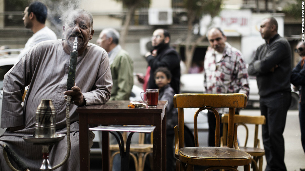 An Egyptian man smokes a waterpipe, known locally as Shisha, as others queue outside a polling station in central Cairo to cast their votes on a new constitution.