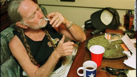 American country singer Willie Nelson takes a drag off a joint while relaxing at his home in Texas, 2000s. A large amount of marijuana is spread out on the table before him 