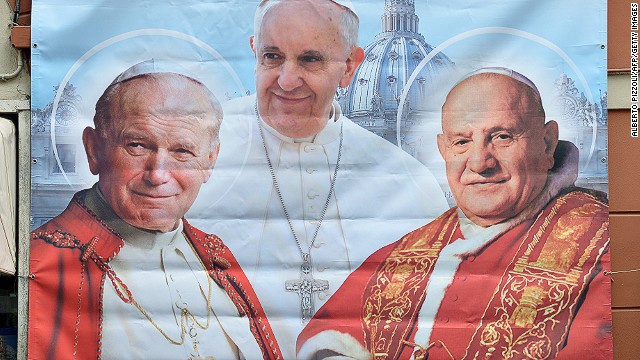 A poster showing Pope Francis middle pope John Paul II (L) and Pope John XXIII (R), that will be canonized next Sunday, is seen in Borgo Pio street near the Vatican during the pontiff weekly general audience in St. Peter's square on April 23, 2014. 