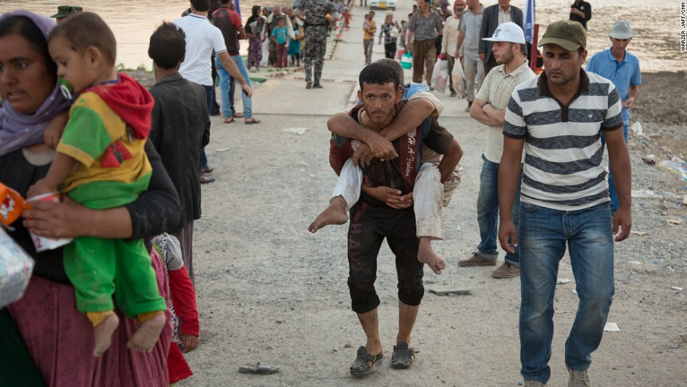 A young refugee carries a disabled man across the bridge.