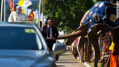 Pope Francis waves to people waiting on the road after crossing a row of decorated elephants standing to welcome him in Colombo, Sri Lanka, Tuesday, January 13, 2015. 