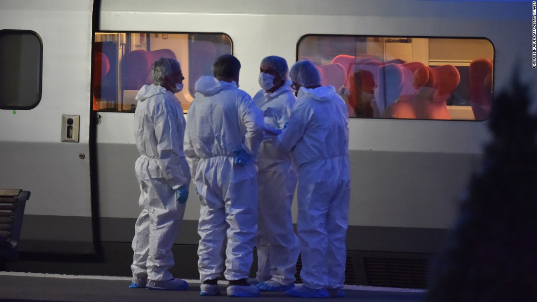 Police in protective suits stand on a platform next to the train. 