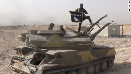 In this image taken from social media, an ISIS fighter holds the group&#39;s flag as he stands on a tank, purportedly captured when they took over the town of Qaryatain, Syria.