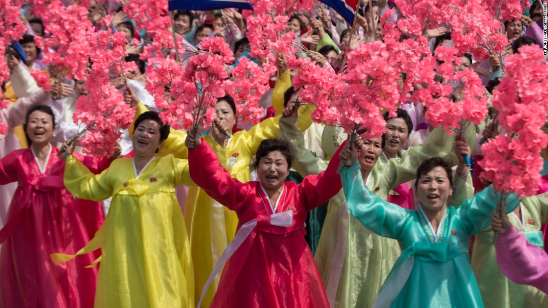 Women wearing traditional Korean dress wave flowers and shout slogans as they pass North Korea&#39;s leader Kim Jong-Un.