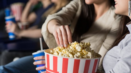 Cropped close up of a woman grabbing popcorn from a bucket watching movies with her female friend at the local cinema food snacks drinks eating enjoyment leisure activity friendship sharing premiere; Shutterstock ID 636925768