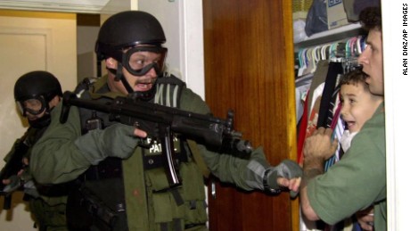 In this third of seven sequential photos, Elian Gonzalez is held in a closet by Donato Dalrymple, one of the two men who rescued the boy from the ocean, right, as government officials search the home of Lazaro Gonzalez for the young boy, early Saturday morning, April 22, 2000, in Miami. Armed federal agents seized Elian Gonzalez from the home of his Miami relatives before dawn Saturday, firing tear gas into an angry crowd as they left the scene with the weeping 6-year-old boy. 
