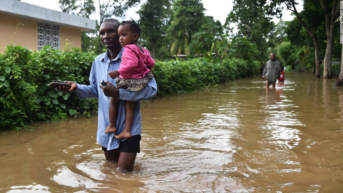A man carries a child through a flooded street in Fort-Liberte, Haiti, on Friday, September 8.