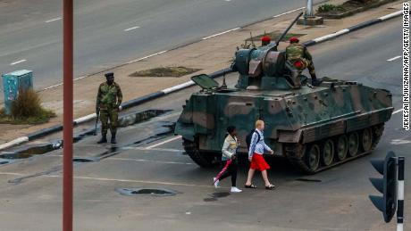 Two pedestrians pass behind an armored personnel carrier stationed at an intersection in Harare on November 15.