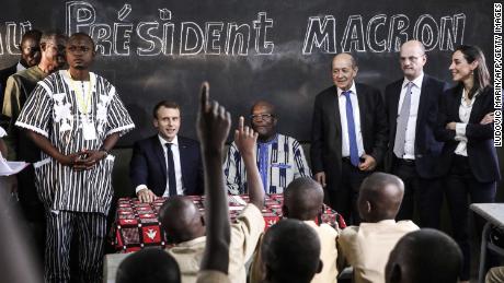 School children rise their hands as French President Emmanuel Macron (left) and Burkina Faso's President Roch Marc Christian Kabore (center) visit a school Tuesday in Ouagadougou.