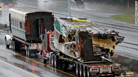 Two damaged train cars sit on flatbed trailers after being taken from the scene of an Amtrak train crash onto Interstate 5.