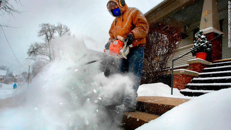 Jose Nieto uses a leaf blower to clear snow from the steps of a sick neighbor during a snowstorm Friday in Bloomington, Illinois.