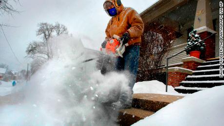 Jose Nieto uses a leaf blower to clear snow from the steps of a sick neighbor during a snowstorm, Friday, Dec. 29, 2017, in Bloomington, Ill. A snow mask and hearing protection allowed him to do his driveway and sidewalks as well. (David Proeber/The Pantagraph via AP)