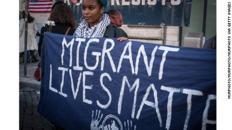 A woman in Rome holds a sign reading &quot;Migrant Lives Matter.&quot;