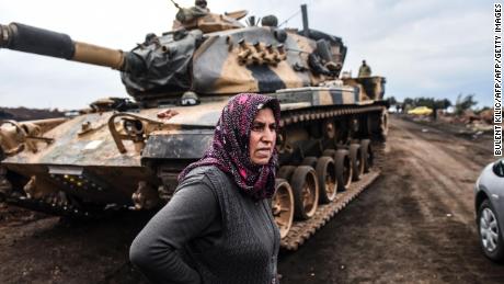 A Turkish villager stands next to Turkish army tanks as soldiers gather close to the Syrian border.