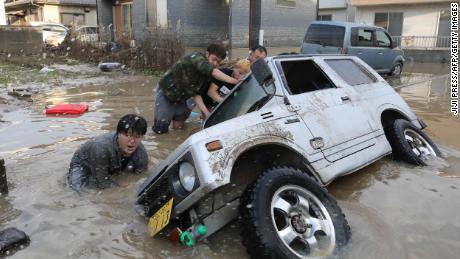 Residents try to upright a vehicle stuck in a flood hit area in Kurashiki, Okayama prefecture on July 9, 2018.