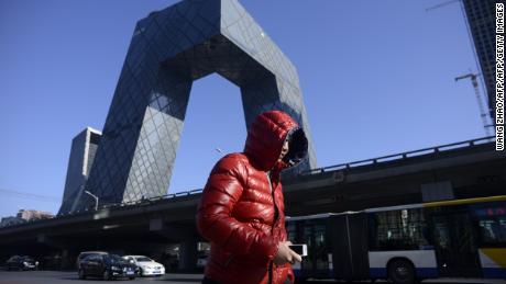 A man walks down the street while the iconic CCTV headquarters looms in the background in Beijing's central business district on January 20, 2017.