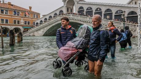 Tourists carry a stroller through the floodwaters near Venice's Rialto Bridge Monday