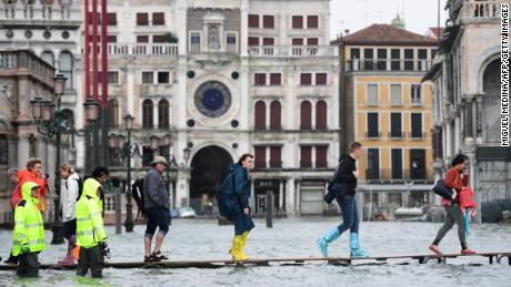 People cross the flooded St. Mark's Square on a raised walkway Monday