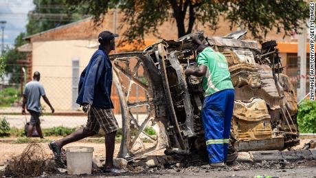 A scrap metal collector saves parts that can be sold from a car that was burned during a protest in Bulawayo on January 17.