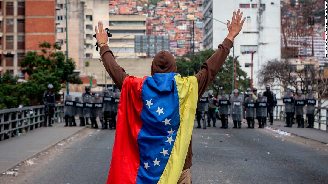 A man wrapped in a Venezuelan flag raises his arms in front of security forces during anti-government protests in Caracas on Wednesday, enero 23.