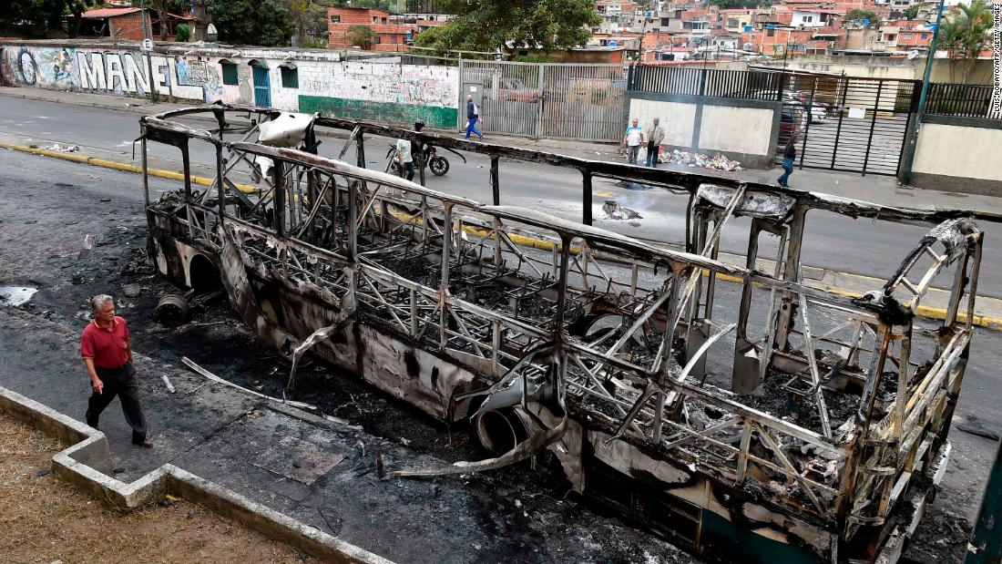 A man walks by a bus that had been set on fire in Caracas.