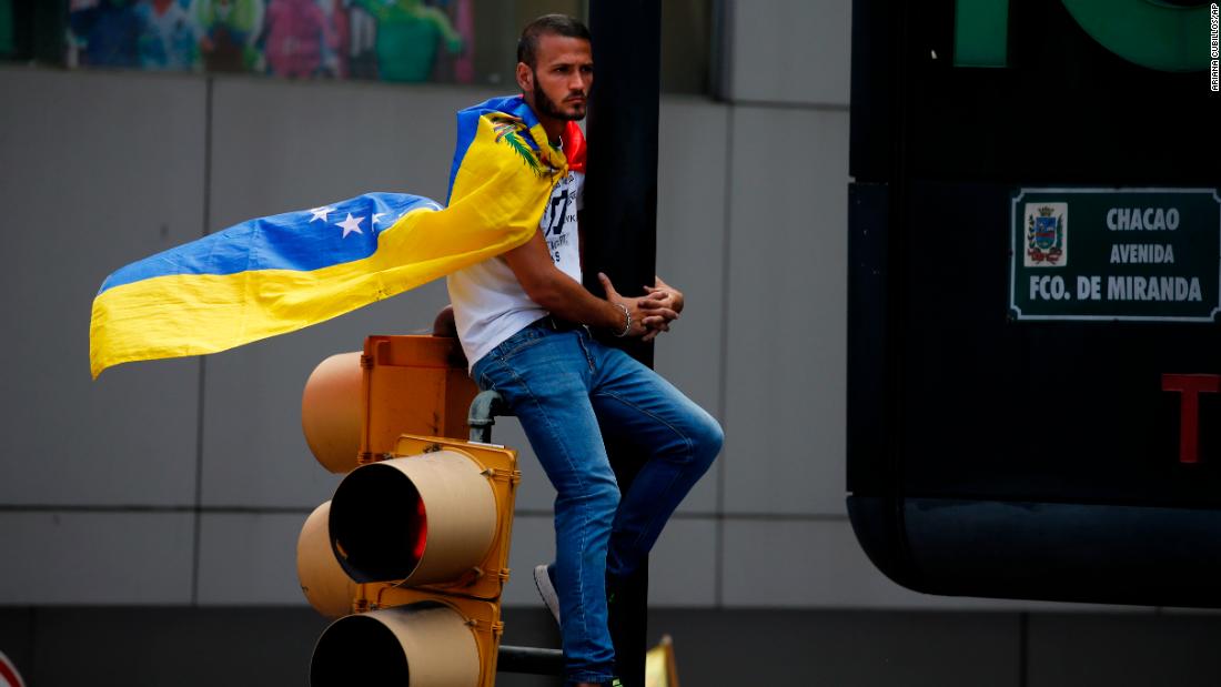 A man wearing a Venezuelan flag sits on a traffic light during the demonstration in Caracas on February 12.