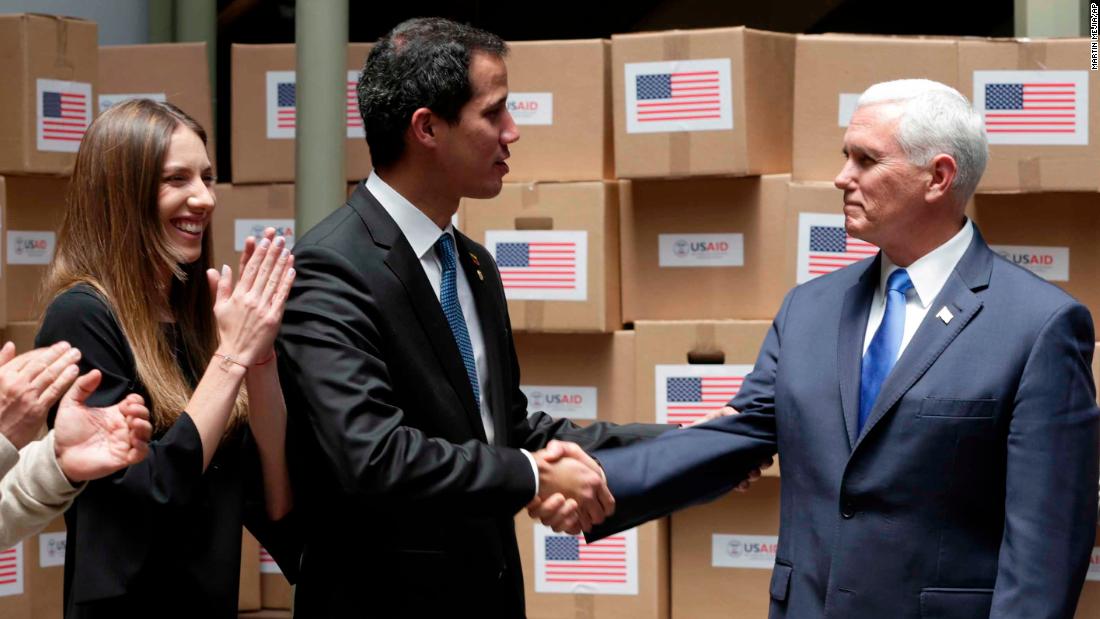 Guaido shakes hands with Pence in Bogota, Colombia, el lunes, febrero 25. The room was filled with humanitarian aid destined for Venezuela. Guaido&#39;s wife, Fabiana Rosales, is pictured at left.