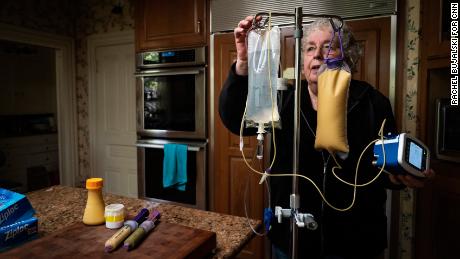 Dafoe is preparing an intravenous infusion bag and feeding tubes in the kitchen of their home.