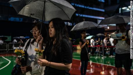 People hold flowers in the rain ahead of a memorial service on July 11, 2019, in Hong Kong, for a protester who died.