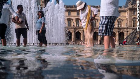 People cool off next to the fountains at the Louvre Museum in Paris.