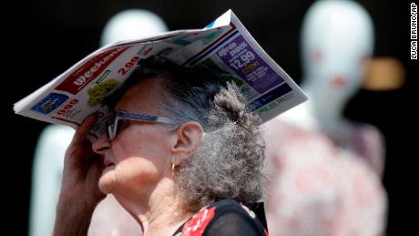 An elderly woman shelters from the hot sun with a newspaper, in Milan, Italy.
