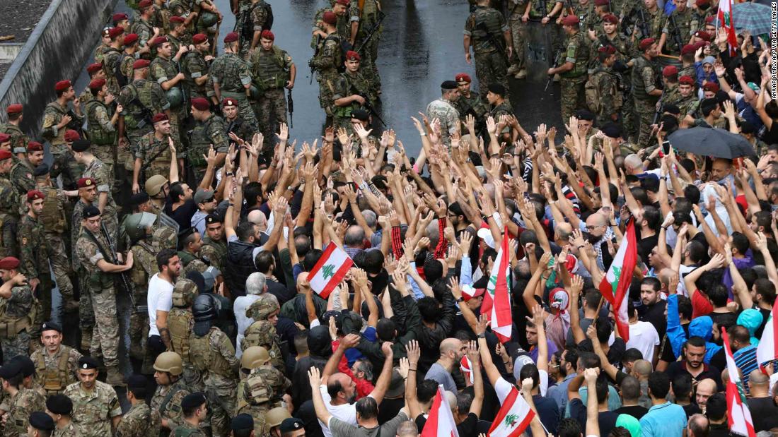 Anti-government protesters wave flags and shout slogans as Lebanese soldiers encircle them on October 23.