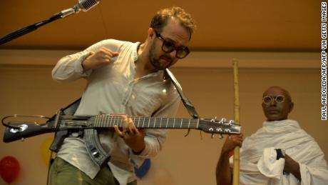 Colombian musician and human rights activist Cesar Lopez (L), plays his "Escopetarra" (mix of the words shotgun and guitar in Spanish), during the celebration of the Gandhi's 146th birth anniversary ,at Memory museum in Medellin, Antioquia on October 2, 2015, as part of the International Day of Non-Violence. AFP PHOTO/Raul ARBOLEDA        (Photo credit should read RAUL ARBOLEDA/AFP via Getty Images)
