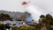 A skycrane drops water on a bushfire burning near houses in Bundoora, Melbourne, on Monday, December 30.