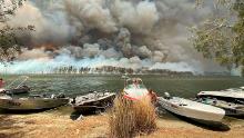 Boats are pulled ashore as smoke and wildfires rage on January 2 behind Lake Conjola.