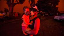 A father holds his daughter as the skies above turn red during the day on January 4 in Mallacoota, Australia. Many parents with young children were stuck in Mallacoota after flights were grounded because of smoke and only school-aged children and older were allowed to evacuate by boat.