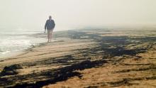 A man walks past ash from bushfires washed up on a beach in Merimbula on January 5.