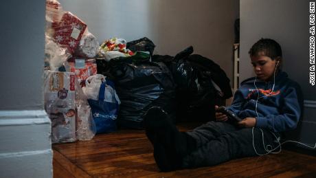 Sebastián Quiñones, 10, watches a video on a phone in a corridor of his aunt&#39;s New York apartment amid a pile of clothing donations for the recent arrivals from Puerto Rico.  