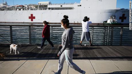 SAN PEDRO, CALIFORNIA - MARCH 27: People wearing face masks walk near the USNS Mercy Navy hospital ship after it arrived in the Port of Los Angeles to assist with the coronavirus pandemic on March 27, 2020 in San Pedro, California. The ship holds 1,000 beds which will be used to treat non-coronavirus patients in an effort to free up hospital beds for those suffering from COVID-19.  (Photo by Mario Tama/Getty Images)