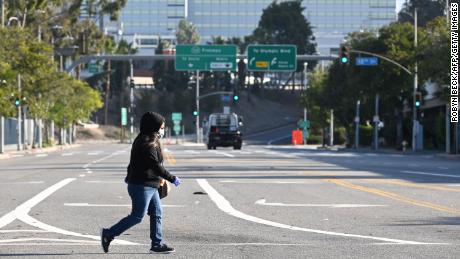 A woman wears a mask as she crosses an empty street near the Los Angeles Convention Center in downtown.