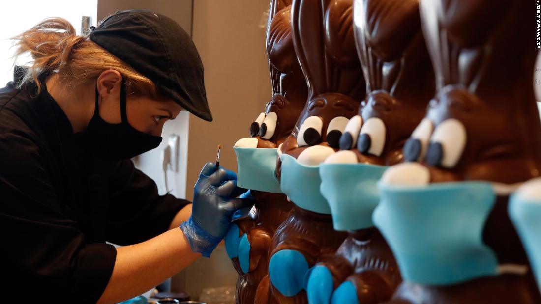 A cake shop employee in Athens, 希腊, prepares chocolate Easter bunnies with face masks on April 8.