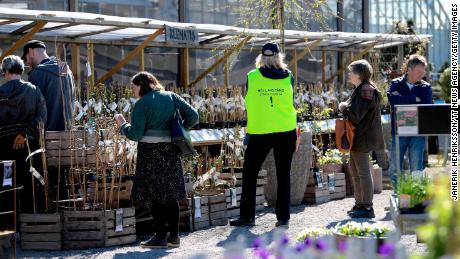 An employee wears a vest reading &quot;Keep distance. Stop Covid-19&quot; as customers look at plants at the Slottstradgarden Ulriksdal garden centre in the Ulriksdal Palace park in Stockholm on April 21.