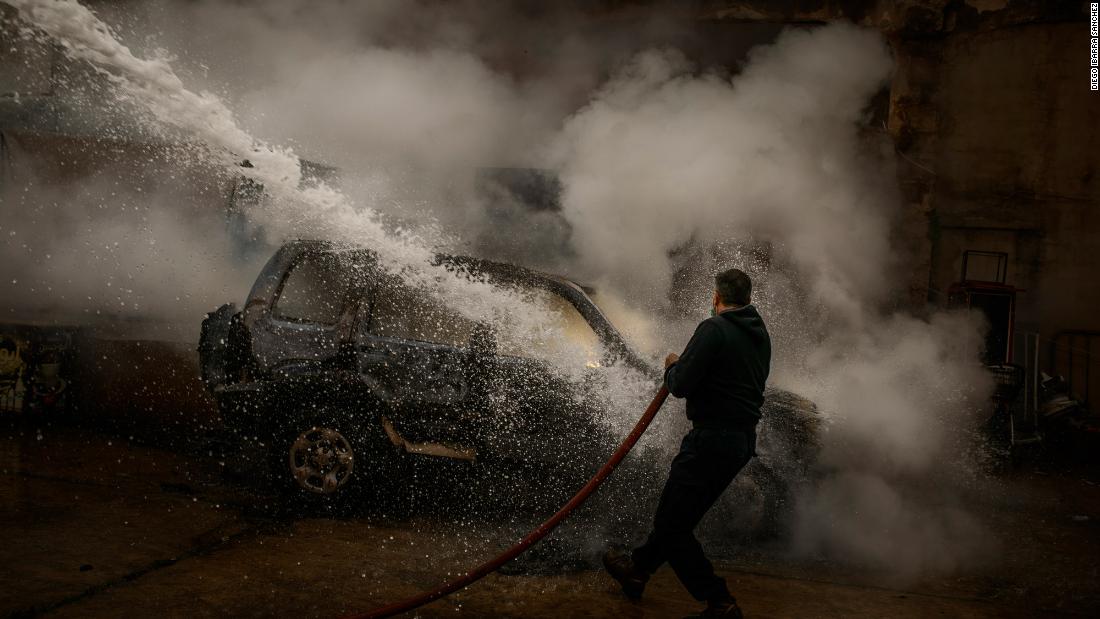 A member of the Lebanese Civil Defense extinguishes a police car that was set on fire by protesters in Tripoli.