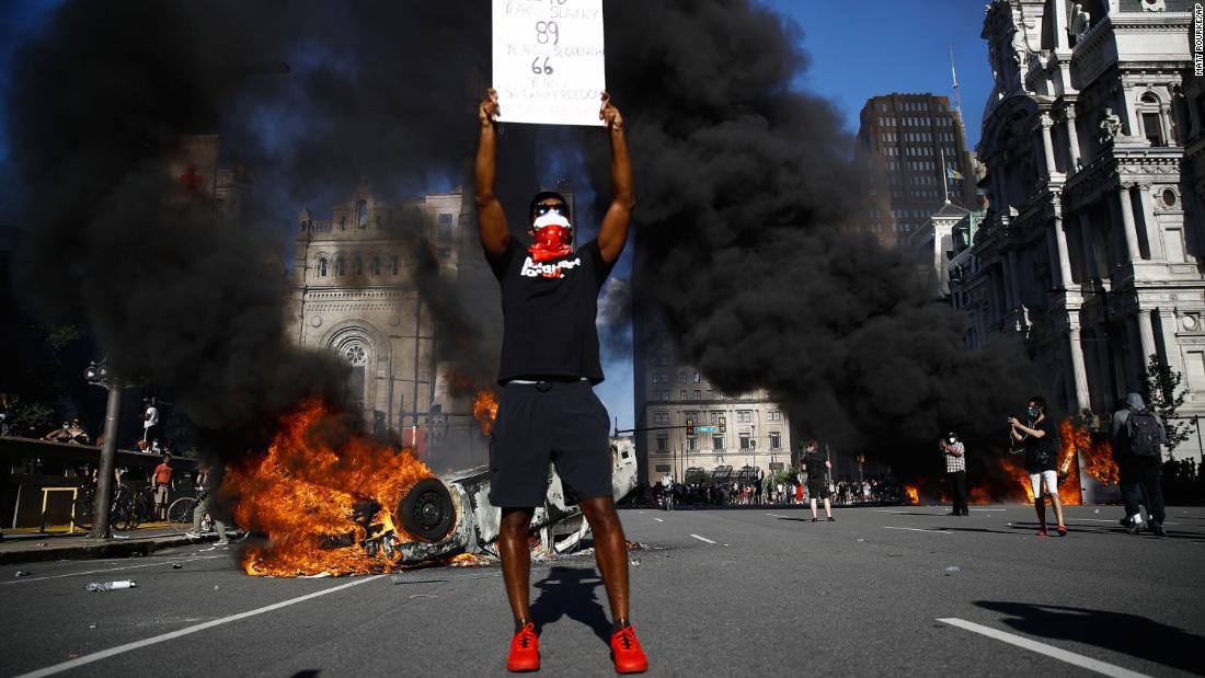 A protester holds a sign while a vehicle burns in a Philadelphia street on May 30.
