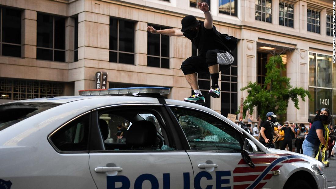 A demonstrator jumps on a police car in Washington, 直流电.