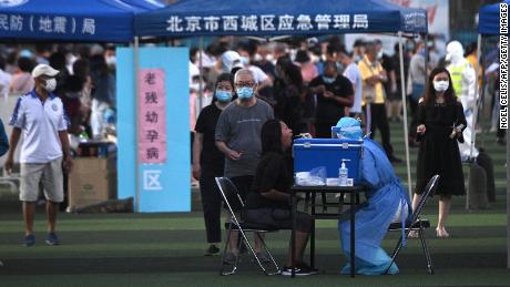 Un trabajador de la salud que usa un traje protector toma una prueba de hisopo de una mujer en un centro de pruebas establecido para personas que visitaron o viven cerca del mercado de Xinfadi en Beijing.