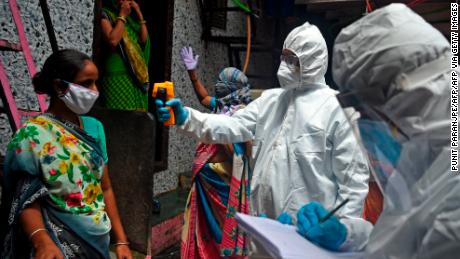 Medizinische Freiwillige, die persönliche Schutzausrüstung (PSA) tragen, messen am 9. Juli 2020 die Temperatur einer Frau im Slum Dharavi in ​​Mumbai. 