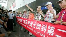 US World War II veterans, including former Flying Tigers, pose for pictures with a banner as a cheering crowd welcome them at the Chongqing Jiangbei Airport on August 18, 2005.